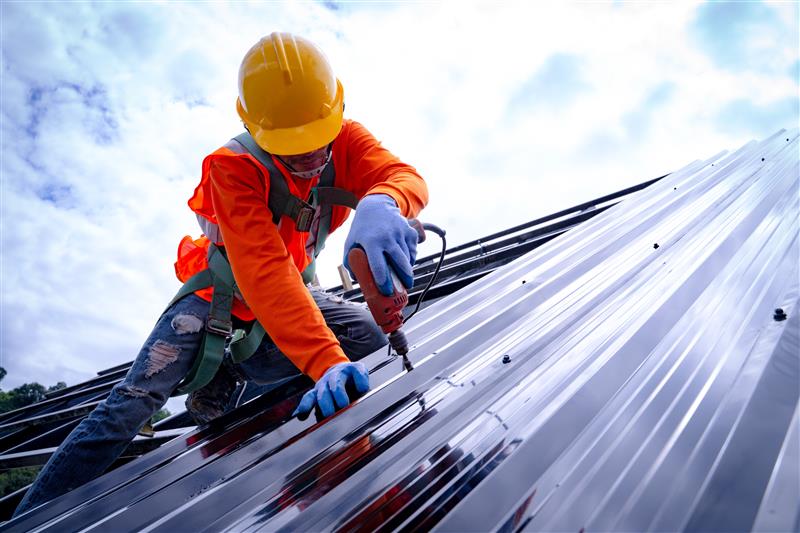 Worker doing his job on the roof, wearing a harness and using a tool. 