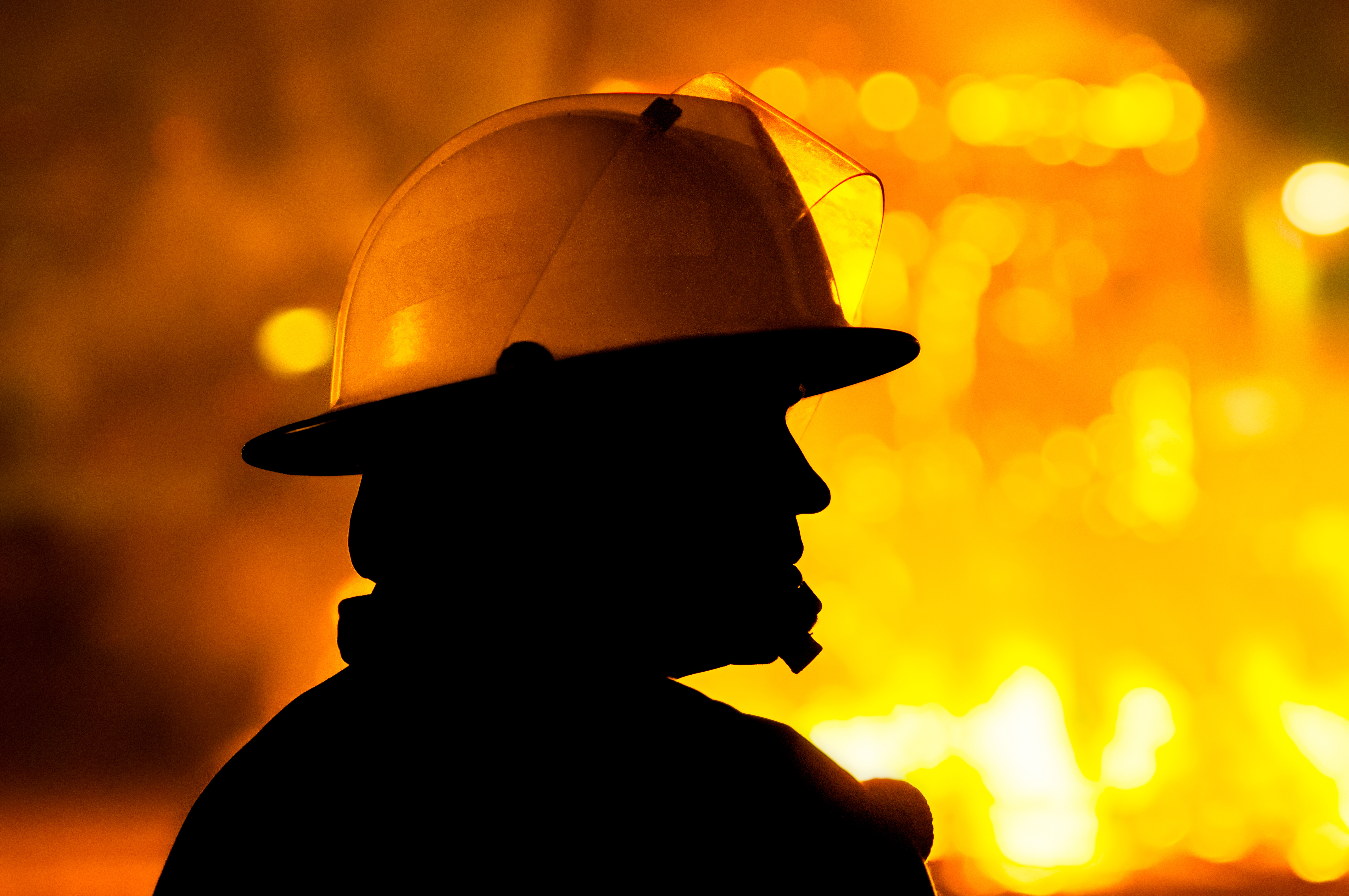 Firefighter standing with fire in the background.